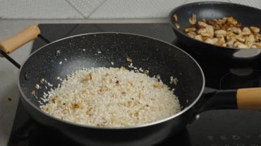 Process of cooking risotto. Cook adds olive oil into arborio rice in frying pan, close up. Italian cuisine dish