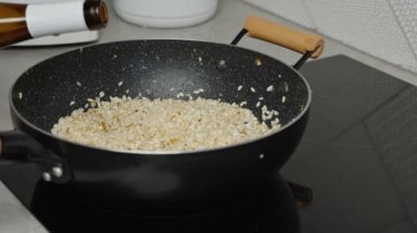 Process of cooking risotto. Cook adds wine into arborio rice in frying pan, close up. Italian cuisine dish