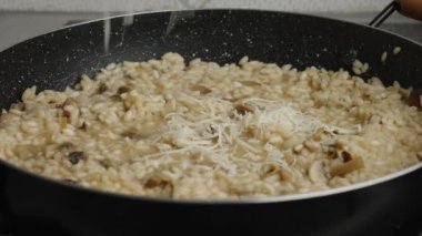 Process of cooking risotto with mushrooms. Cook adds grated cheese into a frying pan with boiled arborio rice, close up. Italian cuisine dish