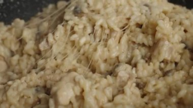 Process of cooking risotto with mushrooms. Cook mixes arborio rice with stretching parmesan cheese in frying pan, close up. Italian cuisine dish