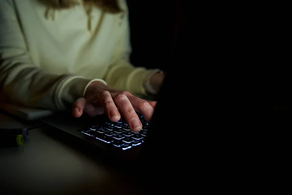 Close up shot of anonymous woman typing on laptop keyboard at night. Online communication and working after hours concept
