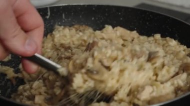 Process of cooking risotto with mushrooms. Cook mixes arborio rice with stretching parmesan cheese in frying pan, close up. Italian cuisine dish