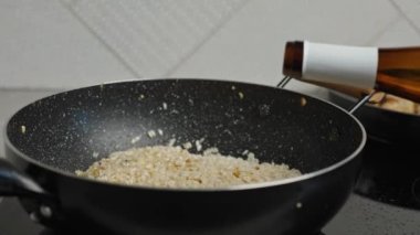 Process of cooking risotto. Cook adds wine into arborio rice in frying pan, close up. Italian cuisine dish