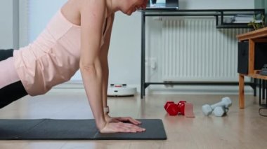 Woman is doing sports exercises in living room. Sport training and fitness concept. Healthy lifestyle for wellness. Woman wearing sportswear does cardio on the floor