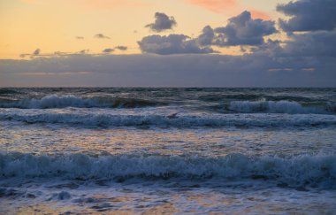 Dalgalarla dolu deniz kıyısı. Gün batımında Baltık Denizi dramatik bulutlu gökyüzüne karşı. Panoramik doğa manzarası