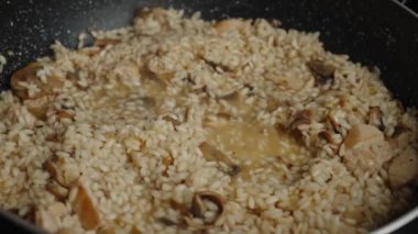 Process of cooking risotto with mushrooms. Arborio rice boiled in frying pan in home kitchen, close up. Italian cuisine dish