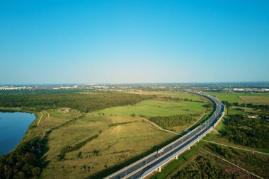 Yeşil tarlaların yakınındaki otoyolda giden arabalar, üst manzara. Kırsal kesimde araba trafiği olan asfalt yolda hava aracı görüntüsü