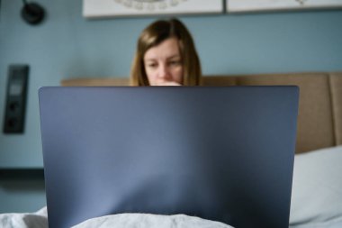 Millennial kadın serbest çalışan yatakta dizüstü bilgisayar kullanıyor. Kadın evde çalışıyor. Rahat bir iş yeri.