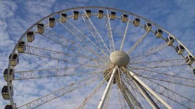 Dönme dolap mavi bulutlu gökyüzünün arka planında döner. Lunapark eğlencesi. Yaz tatili