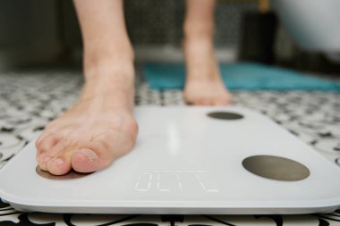 Çıplak ayaklı kadın banyoda tartıya ağırlığını koyuyor. Yerdeki dijital pulları kullanarak ağırlığını ölçen bir kadın..