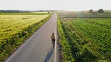 Bisiklet eğitimi aldım. Bisiklet üniforması ve kask giyen erkek sporcu tarla yakınlarındaki kırsal yolda bisiklet sürüyor.