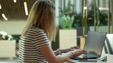 Yeşil bitkilerle birlikte çalışan bir kadın. Laptop klavyesinde yazan serbest çalışan bir kadın. Kafede online çalışma