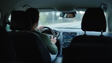 Erkek sürücü araba kullanıyor, içeriden. Şehir caddesinde araba süren, yol trafiğine bakan ve direksiyonu çeviren bir adamın arka görüntüsü. Güvenli sürüş