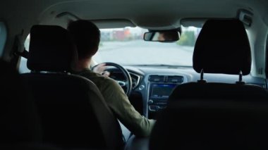 Erkek sürücü araba kullanıyor, içeriden. Şehir caddesinde araba süren, yol trafiğine bakan ve direksiyonu çeviren bir adamın arka görüntüsü. Güvenli sürüş