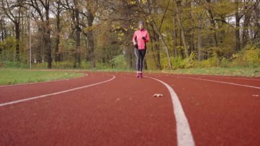 Yarış pistinde koşan kadın. Stadyumda koşan bayan koşucu. Sonbahar günü açık havada aktif spor egzersizleri. Sağlıklı yaşam tarzı