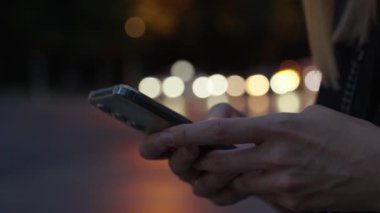 Kadın gece caddesinde akıllı telefon kullanıyor, sosyal medya okuyor ve internette geziniyor. Telefonunu elinde tutan kişi, hareket halindeki arabalarla gece sokağına bastırıyor. Çevrimiçi bağımlılık