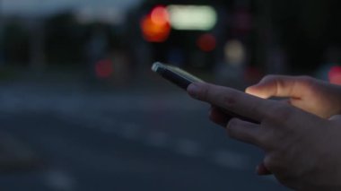 Kadın gece caddesinde akıllı telefon kullanıyor, sosyal medya okuyor ve internette geziniyor. Telefonunu elinde tutan kişi, hareket halindeki arabalarla gece sokağına bastırıyor. Çevrimiçi bağımlılık