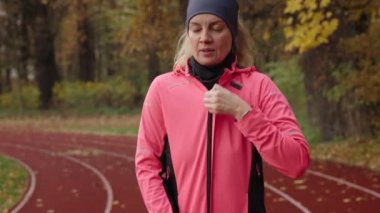 Kadın koşucu koşmaya hazırlanıyor, stadyum koşu bandında spor kıyafetlerini giyiyor. Yolda koşan bir kadın. Sonbahar günü açık havada spor egzersizleri.