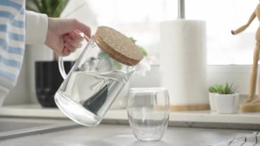 Kadın mutfaktaki sürahiden bardağa temiz su dolduruyor susuzluğunu gideriyor, yaşam tarzı sağlık sigortası kavramı
