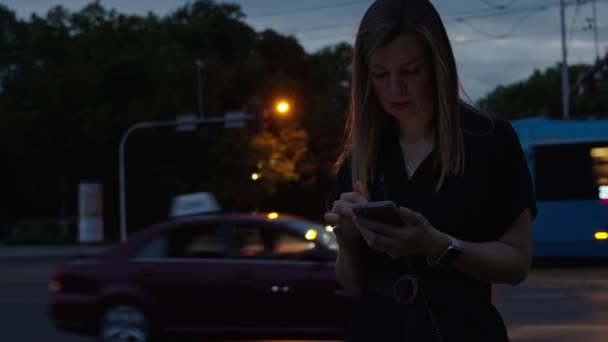 女性は夜通りにスマートフォンを使用し ソーシャルメディアを読み インターネットを閲覧します 人々は携帯電話を握り 移動車で夜通りに表示を押しています オンライン中毒 — ストック動画