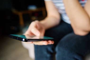 Evde cep telefonu kullanan bir kadın. Kanepede oturan ve akıllı telefondan sosyal ağlara bakan bir kadın.