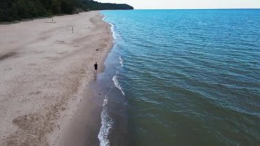Adam sakin mavi denizin yanında kumlu sahilde koşar, hava manzarası