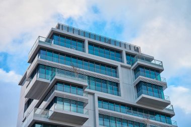 Şehirde bulutlu gökyüzüne karşı çağdaş binalar, balkonları ve cam pencereleri olan modern mimari yapılar..