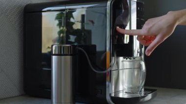Kadın sabahları kahve yapıyor. Kahve makinesindeki kadın eli tuşlara basar, kahve demlemek için program seçer