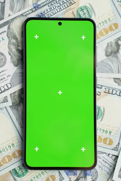 Smartphone with green screen on pile of dollar banknotes, top view. Concept of online earnings