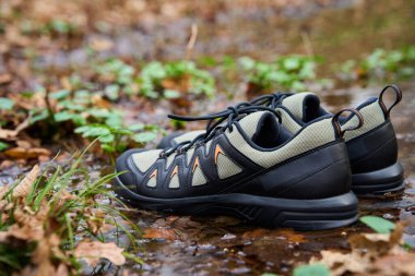 Yürüyüş botları orman zemininde duruyor, su birikintisine batmış, yapraklarla çevrili. Orman zeminine karşı dayanıklı yürüyüş ayakkabıları. Keşif ve açık hava aktiviteleri kavramı