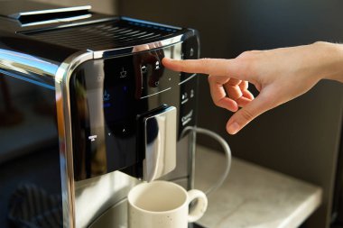 Kadın, modern espresso makinesiyle taze kahve hazırlıyor. Kahve makinesindeki kadın eli düğmeye basıyor.