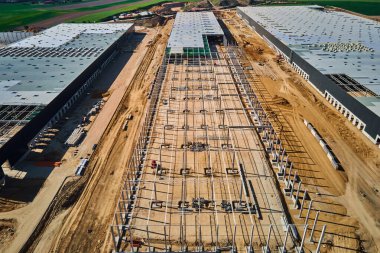 Aerial view of construction site with warehouse building under construction for storage. Assembling industrial building with steel frame structure and roof truss. Infrastructure for logistics clipart