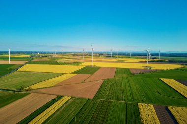 Rüzgâr jeneratörleri renkli tarımsal alanların üzerinde çiçek açan kolza tohumlarıyla. Türbinler rüzgar enerjisini kullanarak elektrik üretir. Yeşil enerji gelişimi