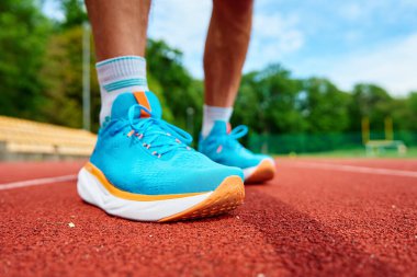 Antrenman sırasında kırmızı stadyum pistinde parlak mavi koşu ayakkabıları giyen bir atlet. Hipodromda spor ayakkabılı sporcu bacakları. Fitness ve sağlıklı yaşam tarzı konsepti