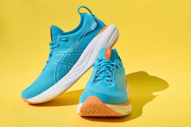 Bir çift mavi Asics Jel-Nimbus 25 spor ayakkabısı ve koyu sarı arka plan gölgesi. Şık ayakkabılar. Modaya uygun minimalizm kavramı