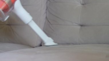 Kadın oturma odasındaki kanepenin yüzeyini temizlemek için portatif kablosuz elektrik süpürgesi kullanıyor. Ev temizliği ve el süpürgesi. Ev işleri.