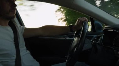 Erkek sürücü araba kullanıyor, içeriden. Gün batımında şehir caddesinde araba süren bir adam yol trafiğine bakıyor ve direksiyonu çeviriyor. Güvenli sürüş