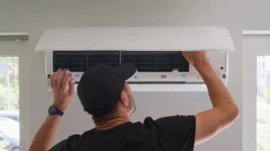 Klima ünitesinin bakımı. Teknisyen, beyaz duvara monte edilmiş klima sistemini kontrol ediyor. Ön kapağı açık olan iklim sistemi iç bileşenleri açığa çıkarıyor. Apartmandaki havalandırma tamir ediliyor.