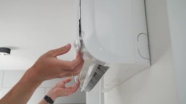Klima ünitesinin bakımı. Teknisyen, beyaz duvara monte edilmiş klima sistemini kontrol ediyor. Ön kapağı açık olan iklim sistemi iç bileşenleri açığa çıkarıyor. Apartmandaki havalandırma tamir ediliyor.