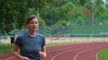 Koşu pistinde koşan bir kadın. Stadyumda bayan koşucu eğitimi. Aktif spor egzersizleri ile sağlıklı yaşam tarzı