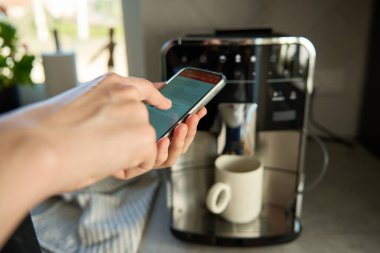 Kahve makinesini çalıştırmak için akıllı telefon uygulaması kullanıyor. Kadın, modern espresso makinesiyle taze kahve hazırlıyor.