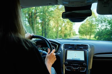 Gün batımında şehir yolunda araba süren bir kadın. Araçtaki kadın sürücünün arka görüntüsü