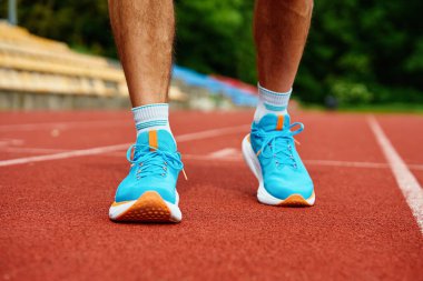 Antrenman sırasında kırmızı stadyum pistinde parlak mavi koşu ayakkabıları giyen bir atlet. Hipodromda spor ayakkabılı sporcu bacakları. Fitness ve sağlıklı yaşam tarzı konsepti