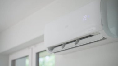 Modern apartmanın beyaz duvarına klima monte edilmiş. Oturma odasında rahat sıcaklık için soğutma sistemi