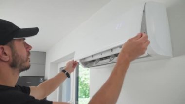Klima ünitesinin bakımı. Teknisyen, beyaz duvara monte edilmiş klima sistemini kontrol ediyor. Ön kapağı açık olan iklim sistemi iç bileşenleri açığa çıkarıyor. Apartmandaki havalandırma tamir ediliyor.