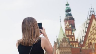 Renkli tarihi binalarla çevrili Avrupa şehir meydanında fotoğraf çeken bir kadın. Kadın turist, seyahat sırasında eski moda kamera ile anıları yakalıyor.