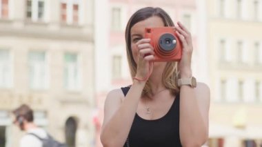 Renkli tarihi binalarla çevrili Avrupa şehir meydanında fotoğraf çeken bir kadın. Kadın turist, seyahat sırasında eski moda kamera ile anıları yakalıyor.