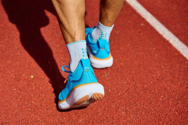 Antrenman sırasında kırmızı stadyum pistinde parlak mavi koşu ayakkabıları giyen bir atlet. Hipodromda spor ayakkabılı sporcu bacakları. Fitness ve sağlıklı yaşam tarzı konsepti