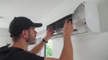 Klima ünitesinin bakımı. Teknisyen, beyaz duvara monte edilmiş klima sistemini kontrol ediyor. Ön kapağı açık olan iklim sistemi iç bileşenleri açığa çıkarıyor. Apartmandaki havalandırma tamir ediliyor.
