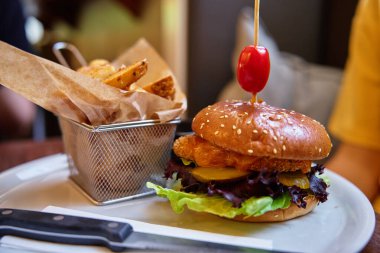 Lokantada beyaz tabakta servis edilen, yanında patates kızartması olan lezzetli tavuk burgerinin yakın çekimi. Fast food ve abur cubur kavramı.